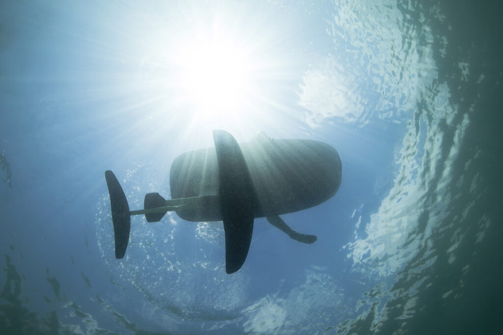 Underwater view of a Fliteboard eFoil rider gliding above the surface on Lake Powell with sunlight streaming through clear blue water